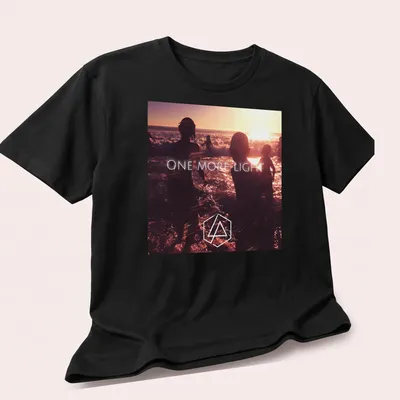 Photographic print of beach silhouettes with 'ONE MORE LIGHT' text in sunset colors. — printed on a unisex t-shirt (angled view)