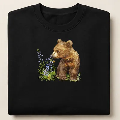 Watercolor bear cub surrounded by vibrant flowers in brown, green, purple, and yellow — printed on a unisex sweatshirt