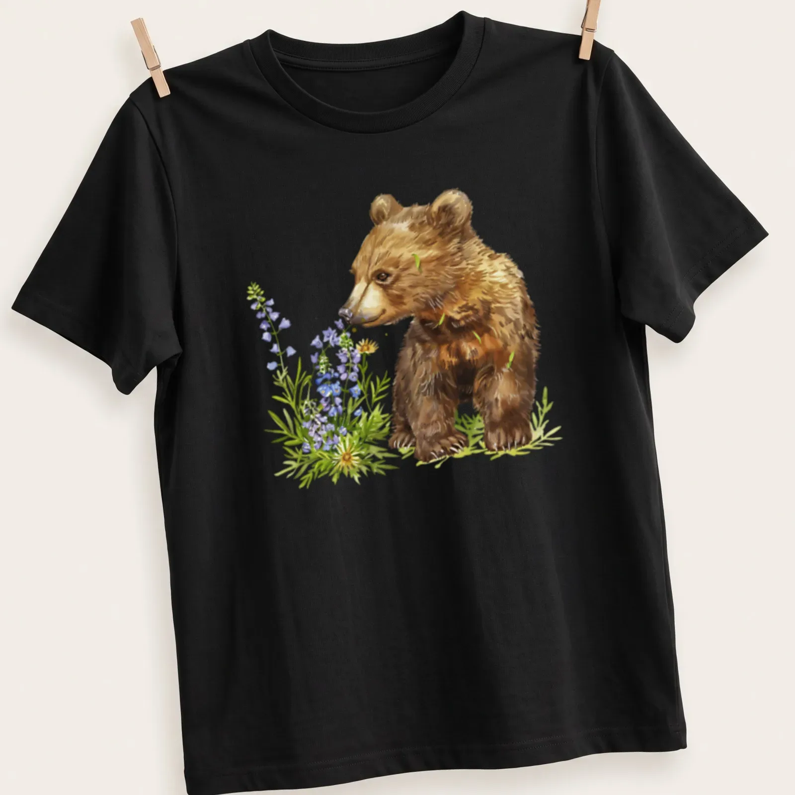 Watercolor bear cub surrounded by vibrant flowers in brown, green, purple, and yellow — printed on a unisex t-shirt