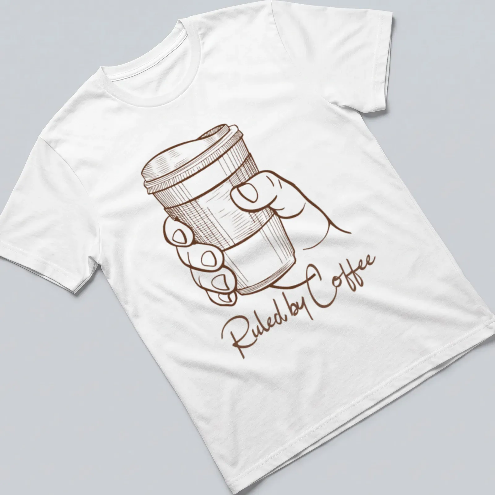 Line art of a hand holding a coffee cup with text 'Ruled by Coffee' in brown and white — printed on a unisex t-shirt