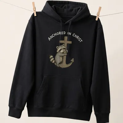 Kawaii illustration of a cute raccoon hugging an anchor with text Anchored in Christ — printed on a unisex hoodie
