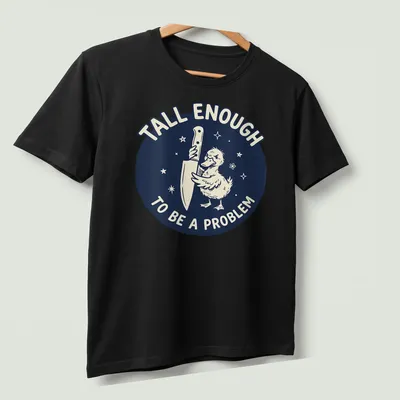 Cartoon duck holding a knife with text reading 'Tall Enough To Be A Problem' in navy and white — printed on a unisex t-shirt (angled view)