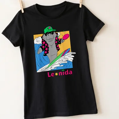 Cartoon manatee surfing with the text 'I ❤️ VACATION' in bright colors — printed on a women's shirt