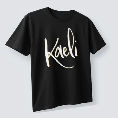 Elegant script personalized name T-shirt featuring 'Kaeli' in gold and white — printed on a unisex t-shirt (angled view)