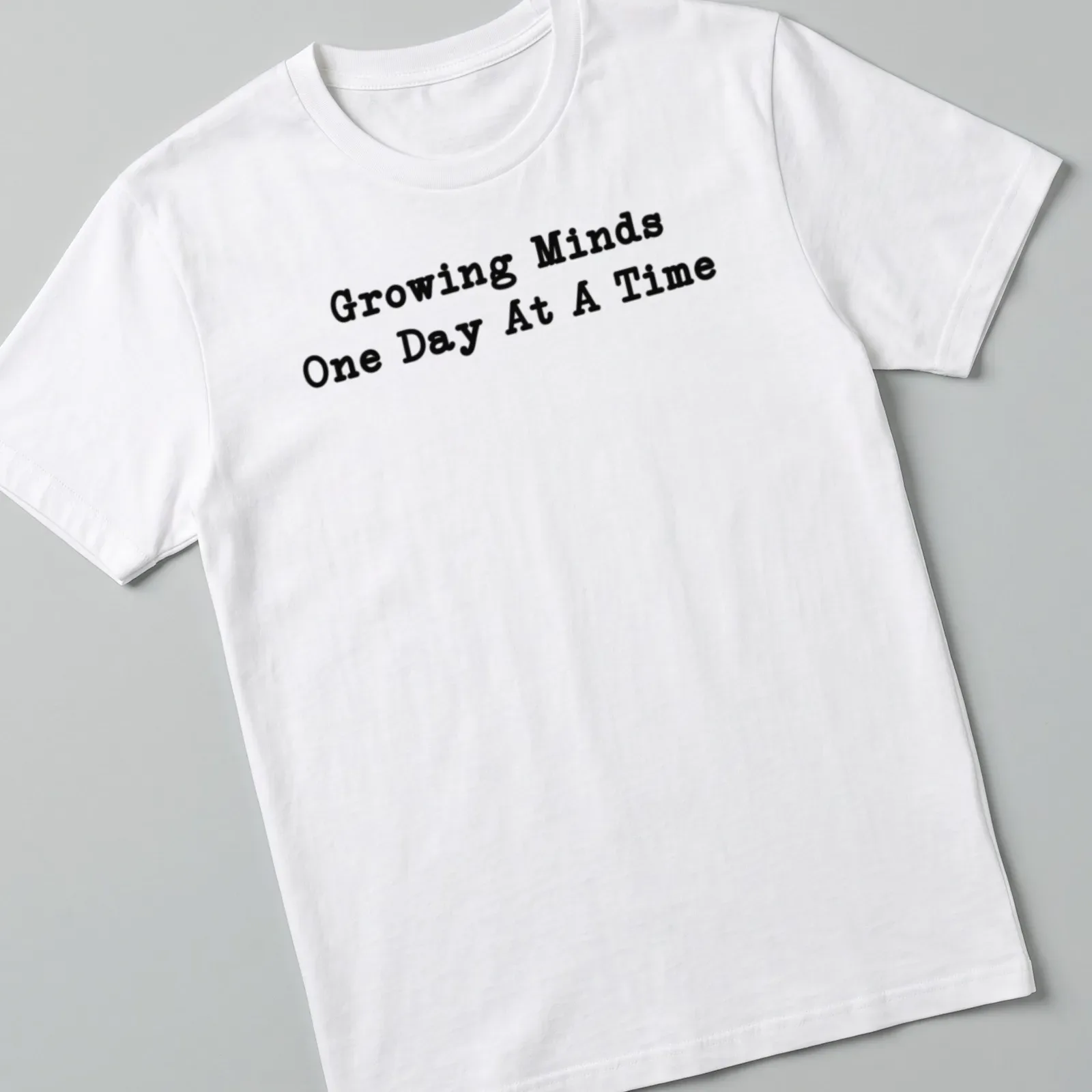 Bold typography Teacher shirt with the phrase Growing Minds One Day At A Time in black — printed on a unisex t-shirt